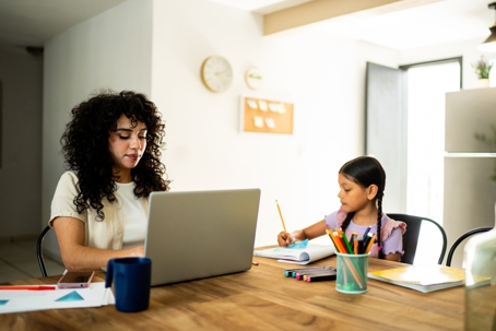 Mother working on their laptop with daughter next to her