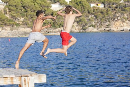 boys jumping off of a dock into a lake
